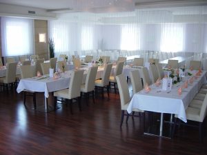 Heller Saal mit gedeckten Tischen und weißen Stühlen